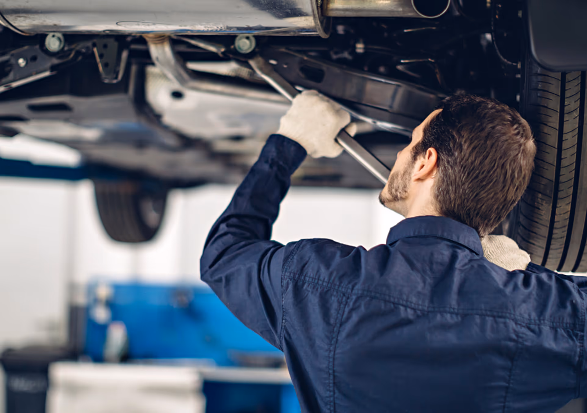 Mechaniker repariert die Unterseite eines Autos in einer Werkstatt.