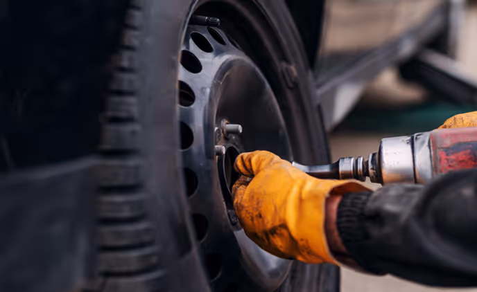 Person mit gelben Handschuhen montiert ein Autoreifen mit einem elektrischen Schlagschrauber.