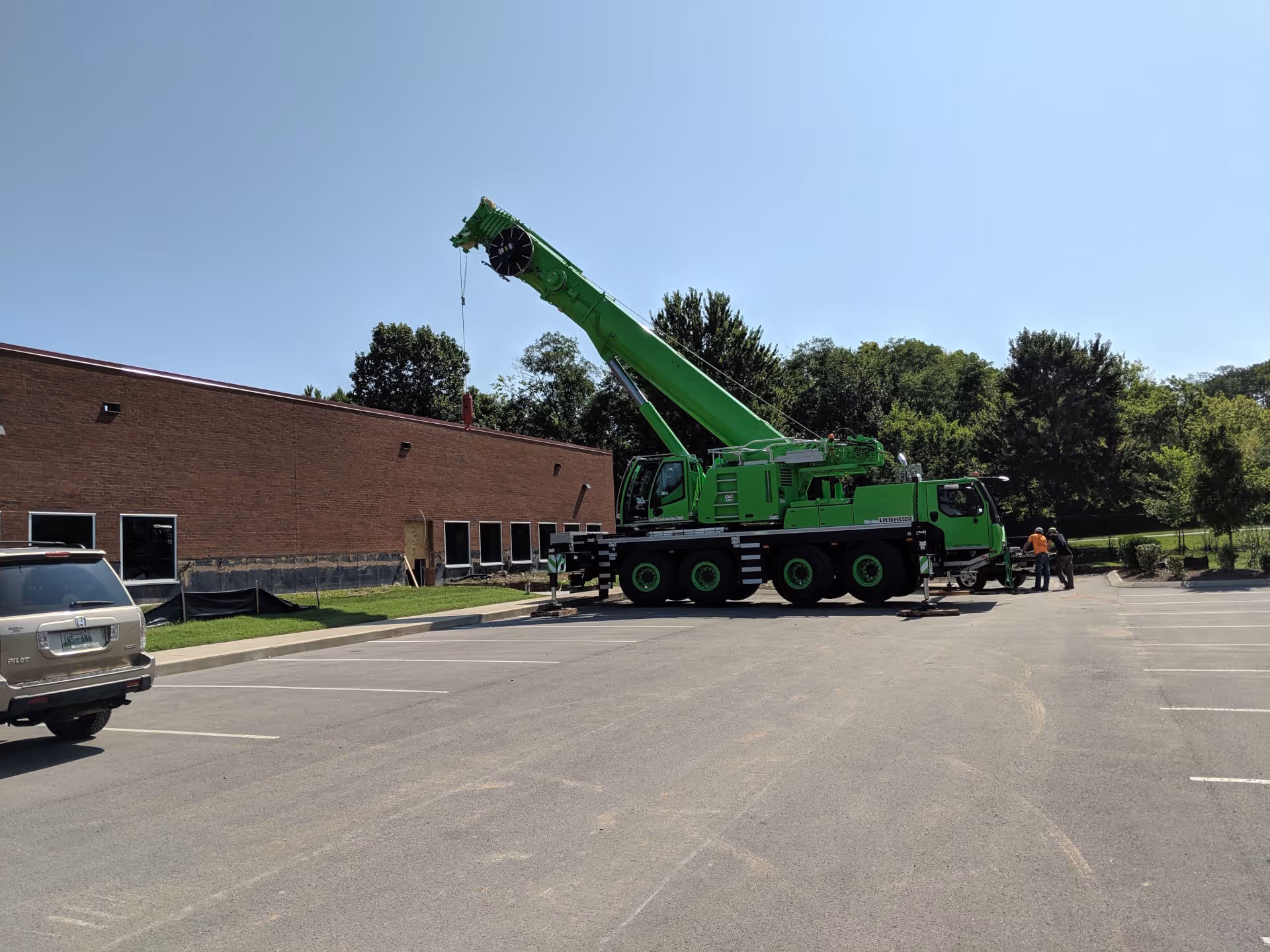 Worker on a green scissor lift installing a large ceiling fan in a warehouse with flags hanging in the background.