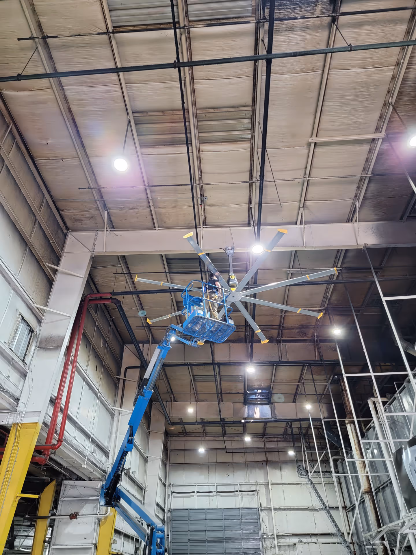 Industrial factory with workers operating machinery and a worker elevated on a blue lift platform.