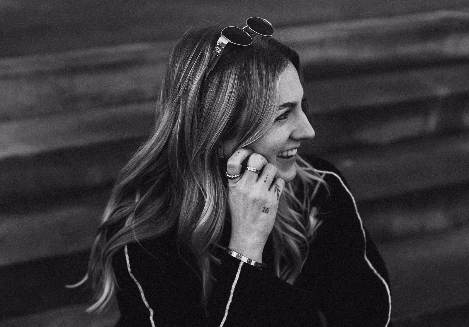 Schwarz-weiß-Porträt einer lächelnden Frau mit langen Haaren, die eine Sonnenbrille auf dem Kopf trägt.