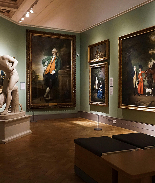 Art gallery room with classical paintings in ornate frames on green walls and a marble statue on a pedestal.