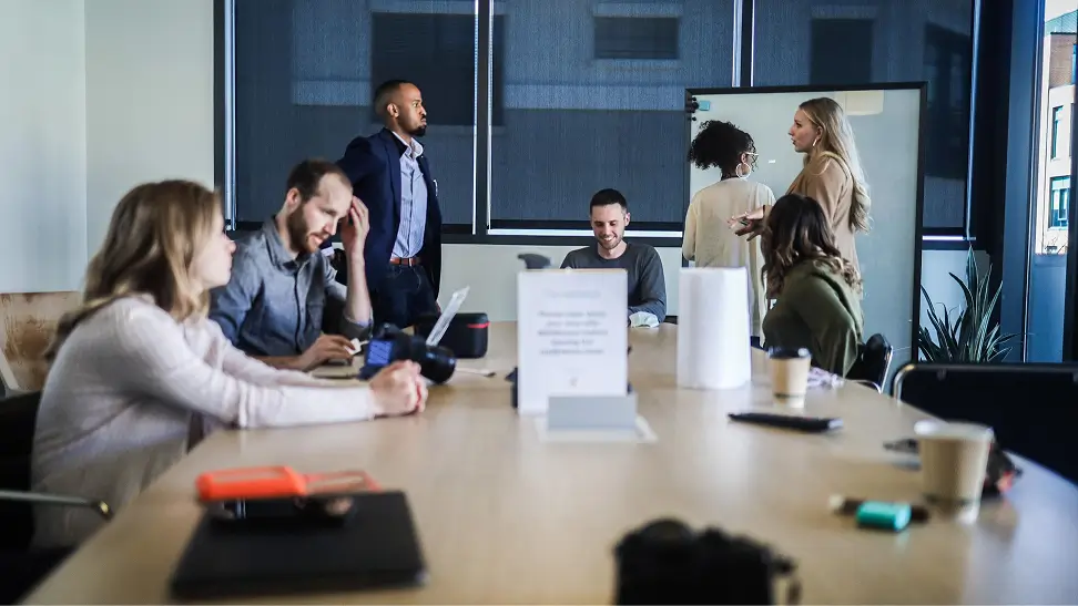 A group of six diverse coworkers engaged in a meeting around a table in a modern office.