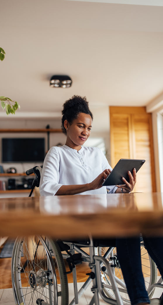 Woman sitting in a wheelchair using a tablet in a bright living room.