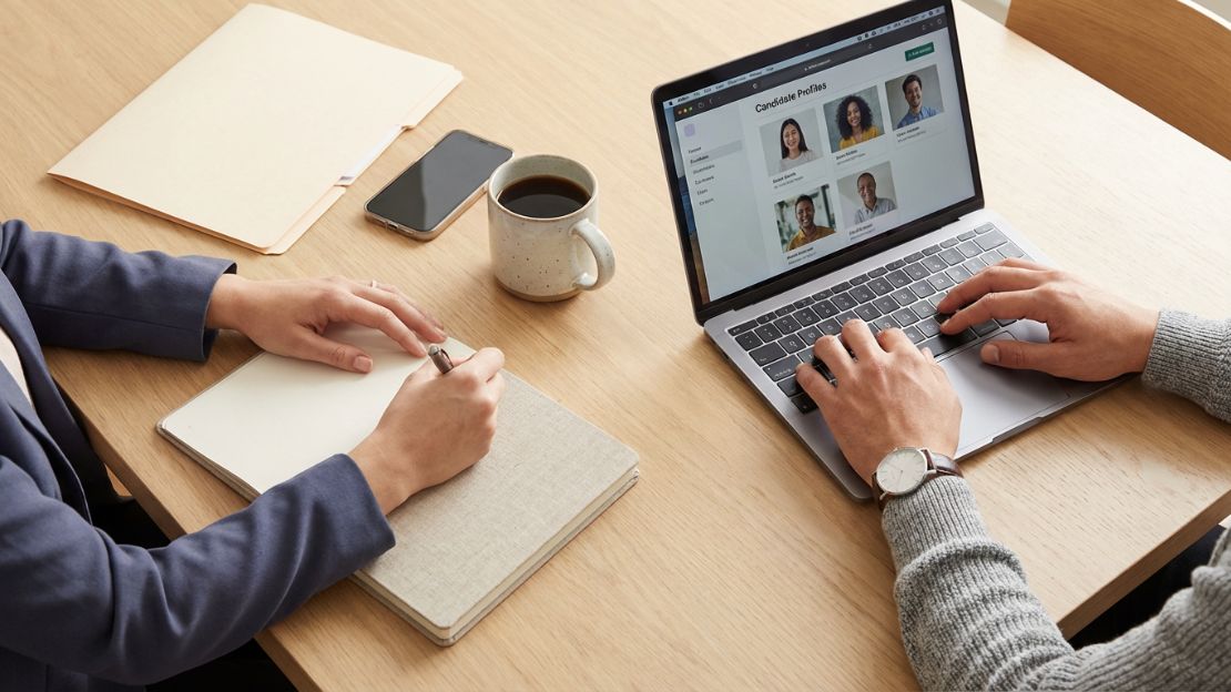Top-down view of two professionals reviewing candidate profiles and taking notes at a clean modern workspace.