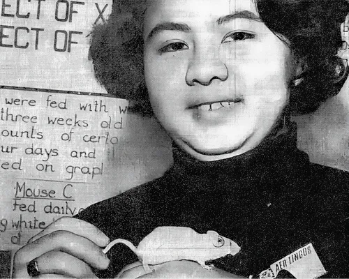 Black and white photo of a young student holding a white mouse for a science project display.