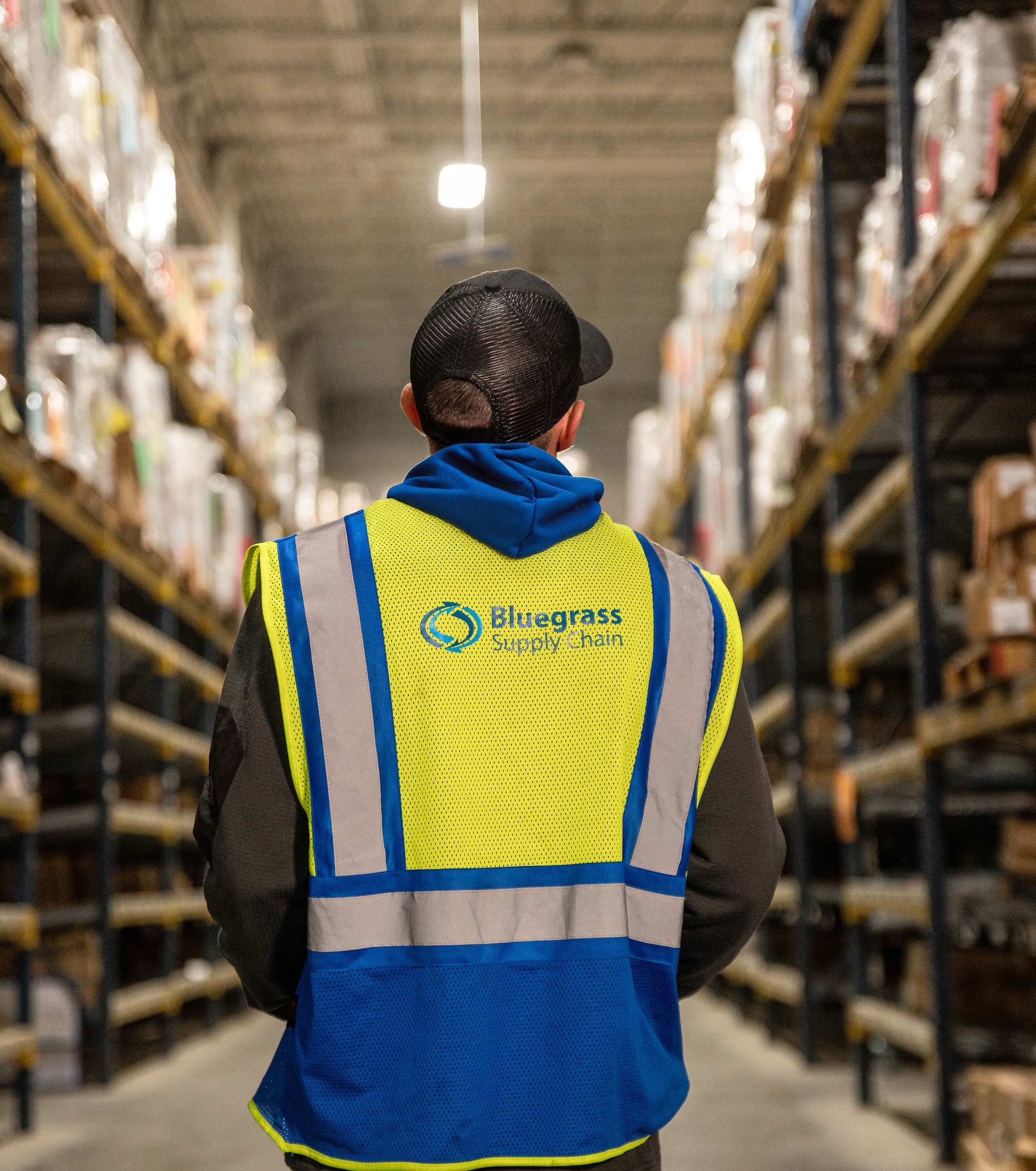 Warehouse worker in a high-visibility vest operating an autonomous robot with bins for sorting or transporting items.