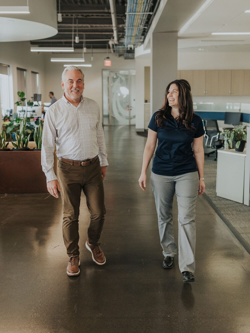 Smiling woman with long light brown hair wearing a navy Bluegrass Supply Chain shirt against a light background.