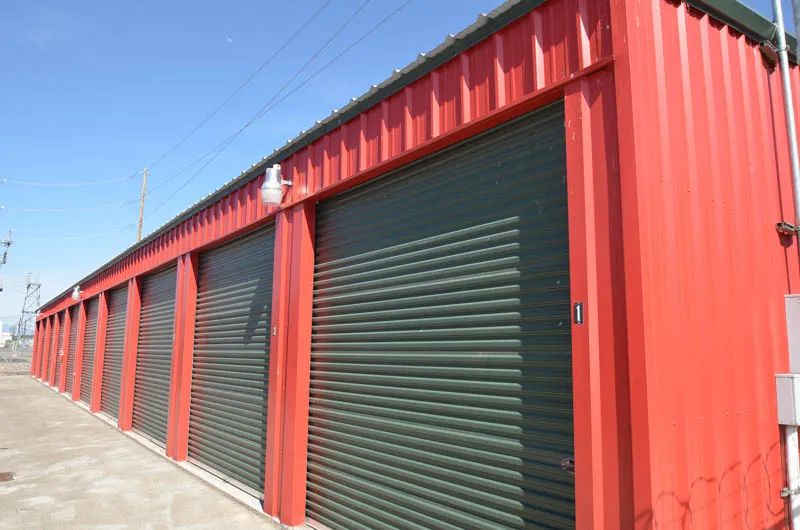 Row of red storage units with green roll-up doors at Security 1st Storage, Pacific Avenue, solid steel construction under clear sky.