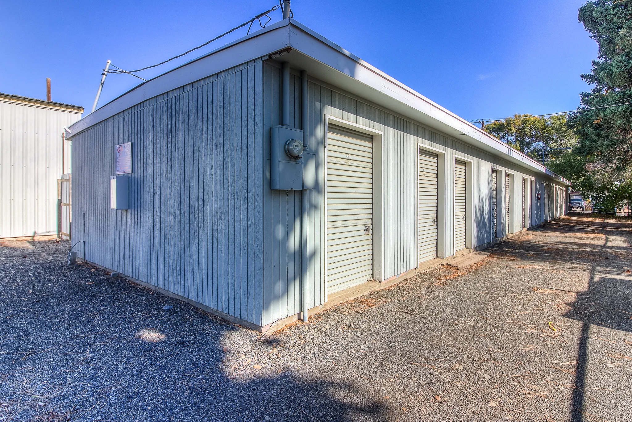 Side view of 34th Avenue storage building at Security 1st Storage with multiple unit doors, gravel pathway, and shaded secure access area.