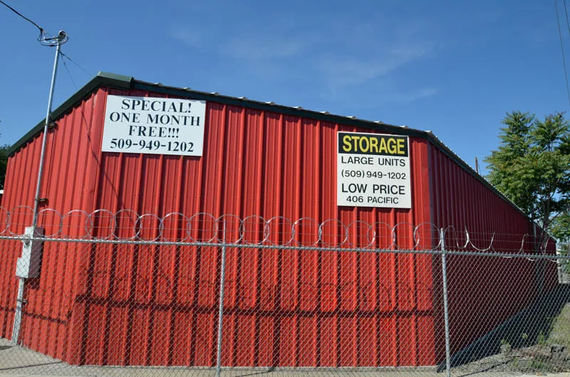 Security 1st Storage Pacific Avenue, exterior wall with promotions and STORAGE sign behind a high, razor-wire security fence.