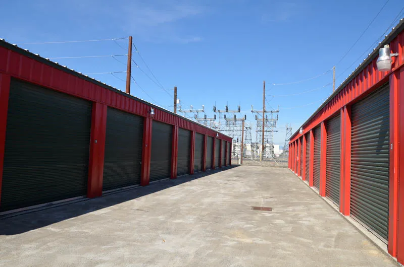 Wide drive aisle between two secure rows of red units with green doors, Pacific Avenue location, bright daylight and clear visibility.