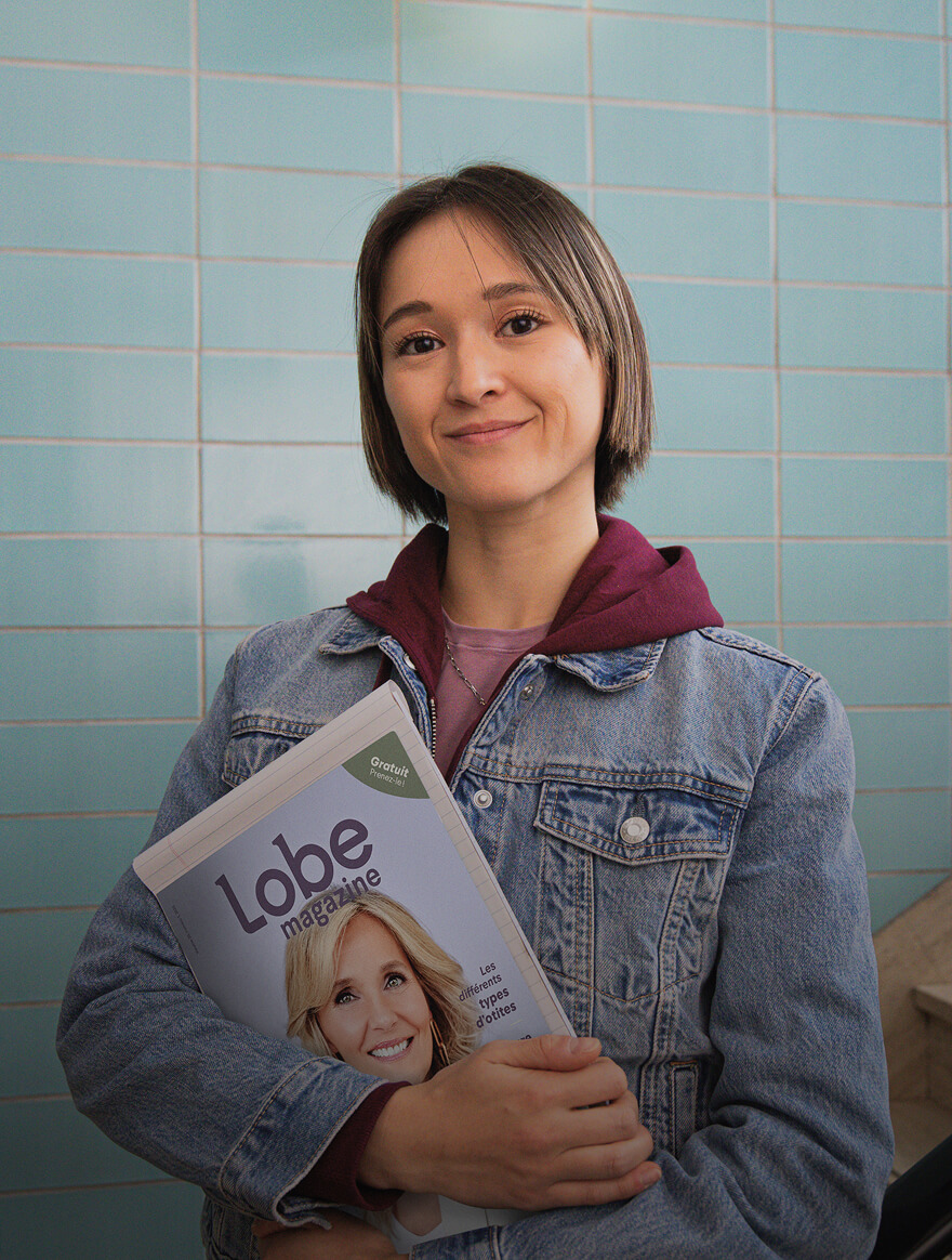 Young woman with short brown hair wearing a denim jacket and maroon hoodie, smiling and holding a copy of Lobe magazine.