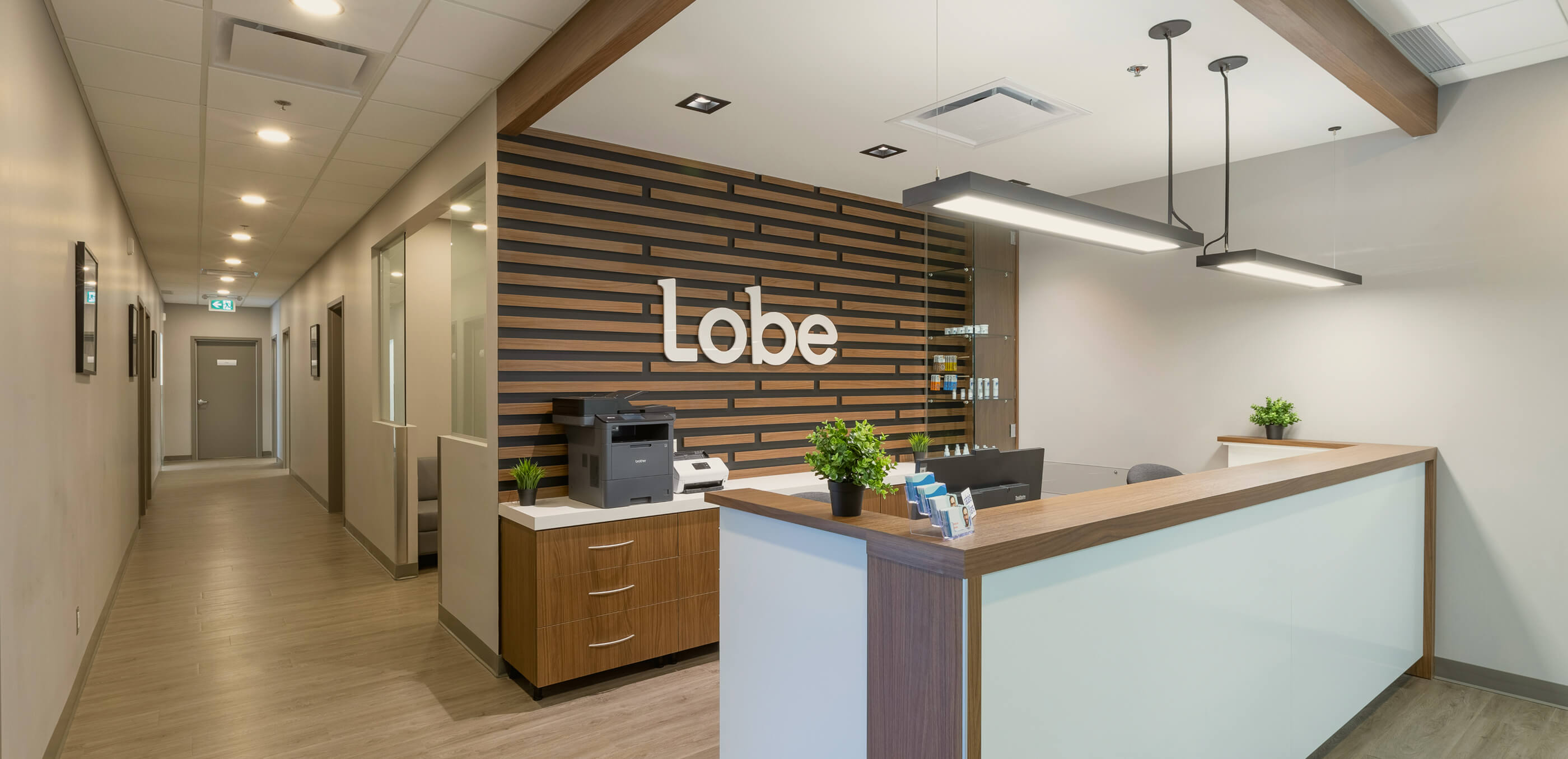 Reception area with modern wooden desk, decorative plants, and a wall featuring the word 'lobe' in white letters on a wooden striped background.