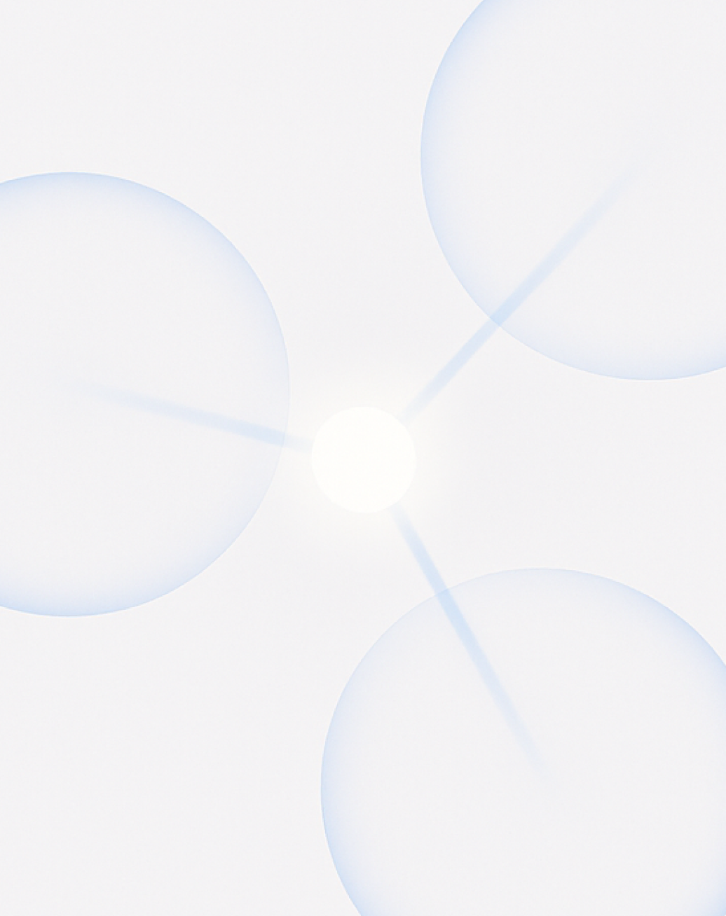 Three large translucent lavender-blue circles arranged around a glowing white center point on a pale gray background, with subtle light rays extending between them, creating a soft pinwheel-like composition.