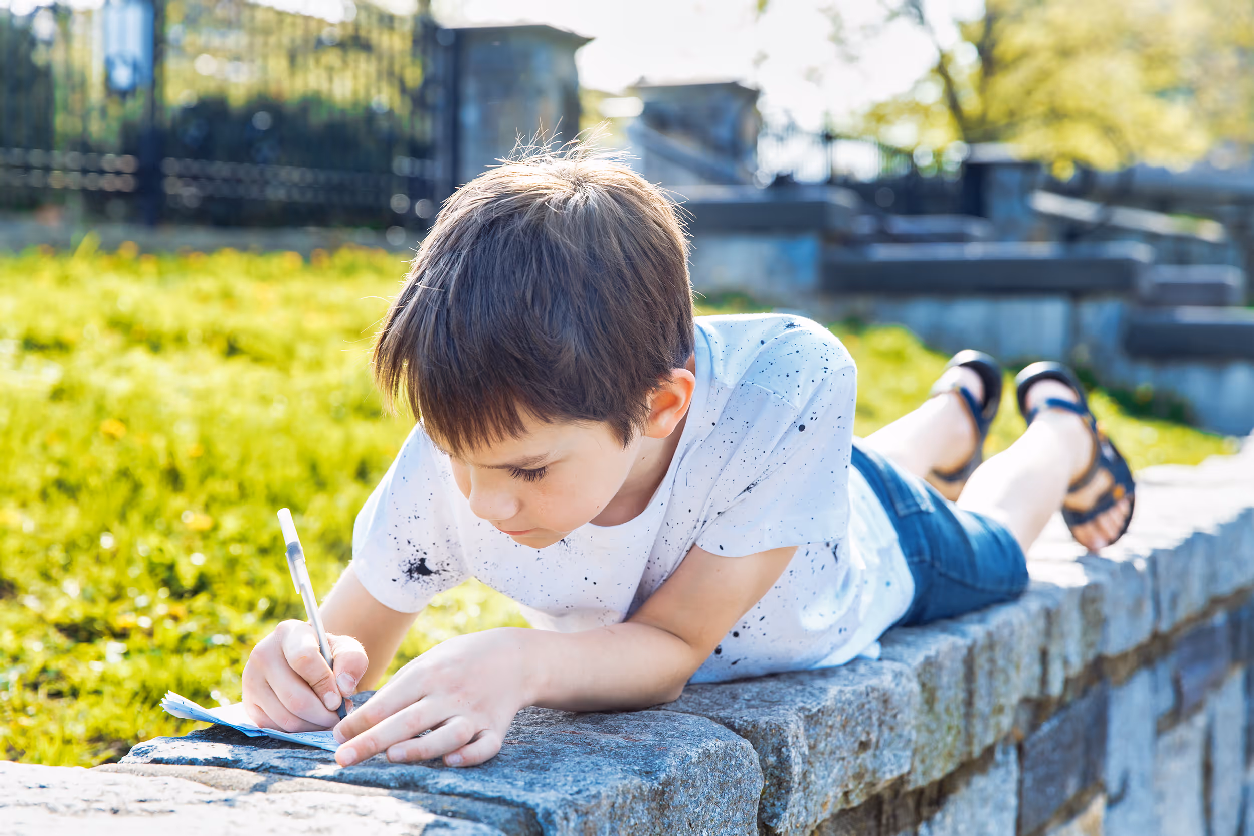 Boy lying down writing outdoors, focused on a learning task for a psychoeducational evaluation