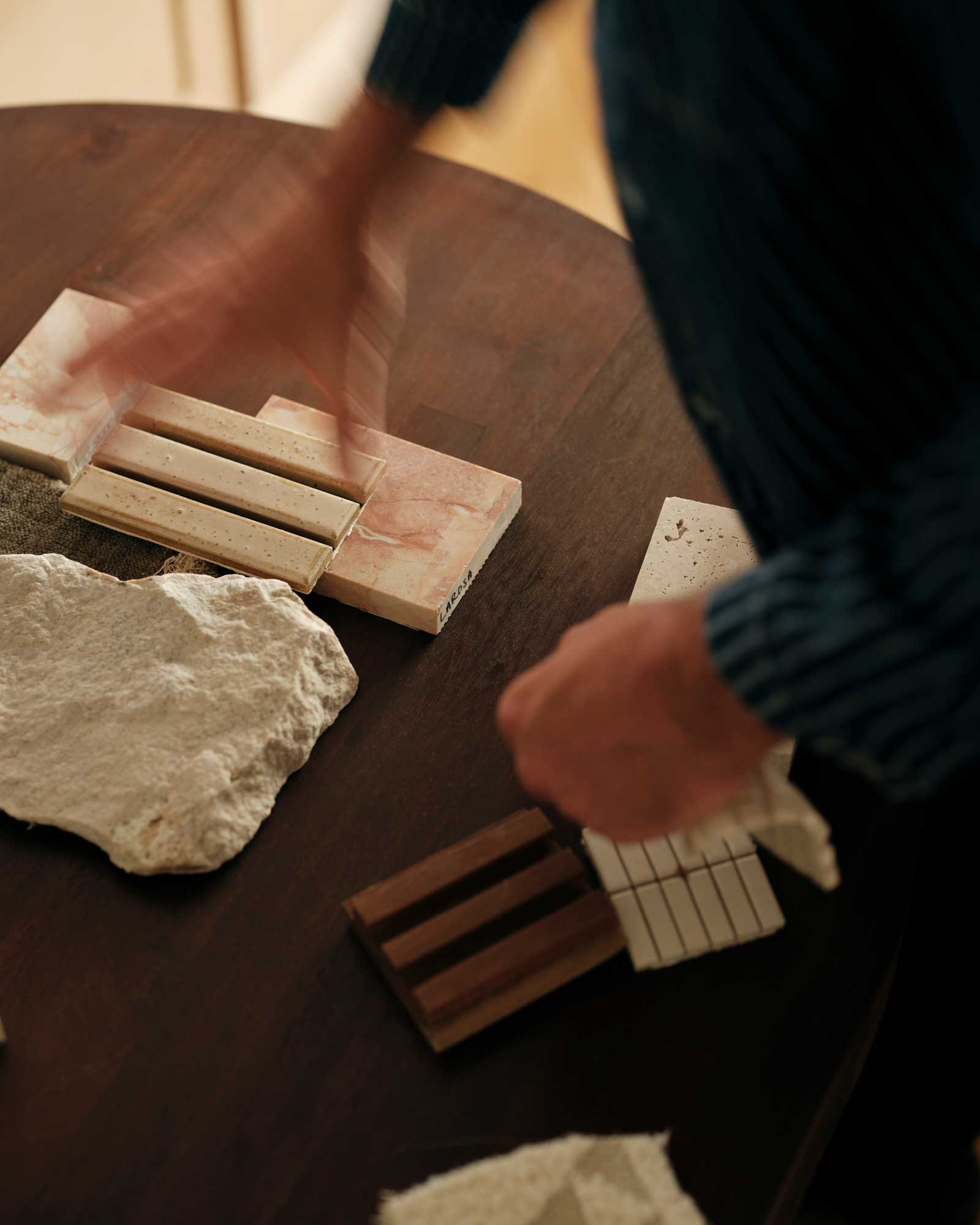 Interior designer arranging various stone and wood samples on a dark wooden table.