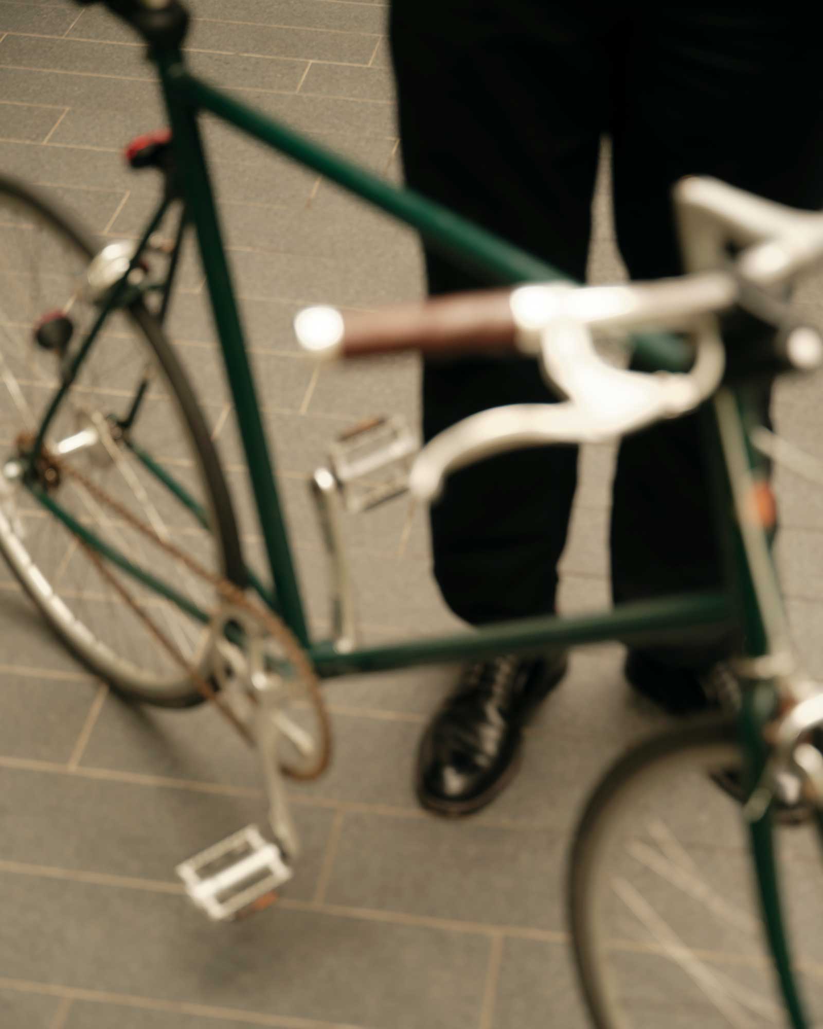 Person standing behind a green bicycle on gray tiled pavement.