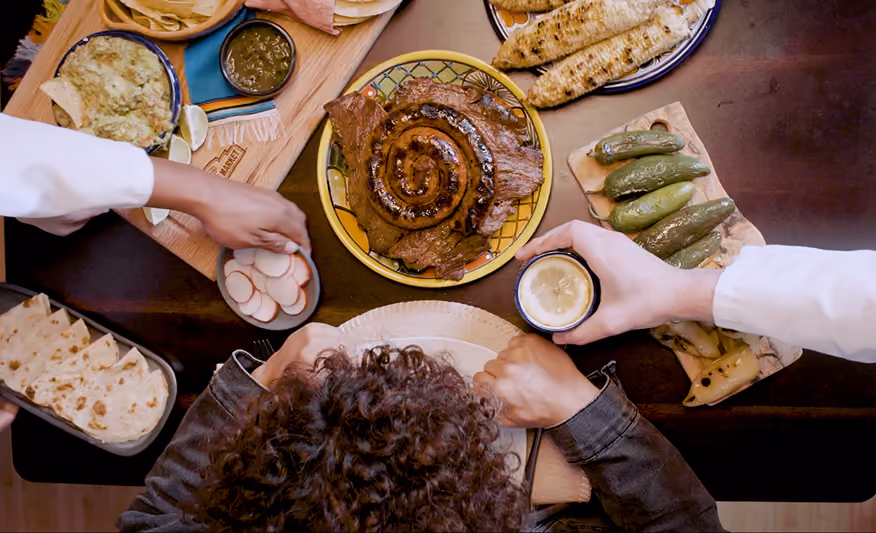 Overhead view of a meal with grilled meat, corn, peppers, radish slices, and tortillas being served.