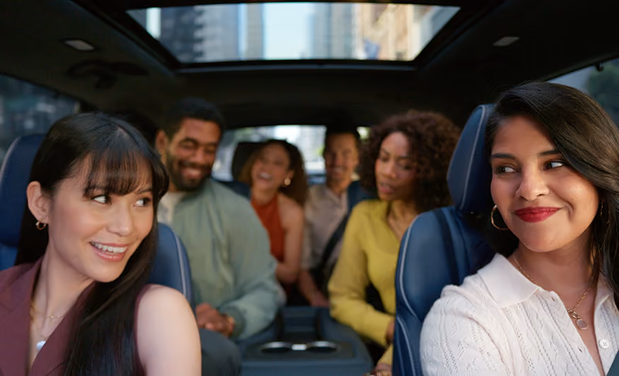 Six diverse friends smiling and chatting inside a car with a sunroof on a city street.
