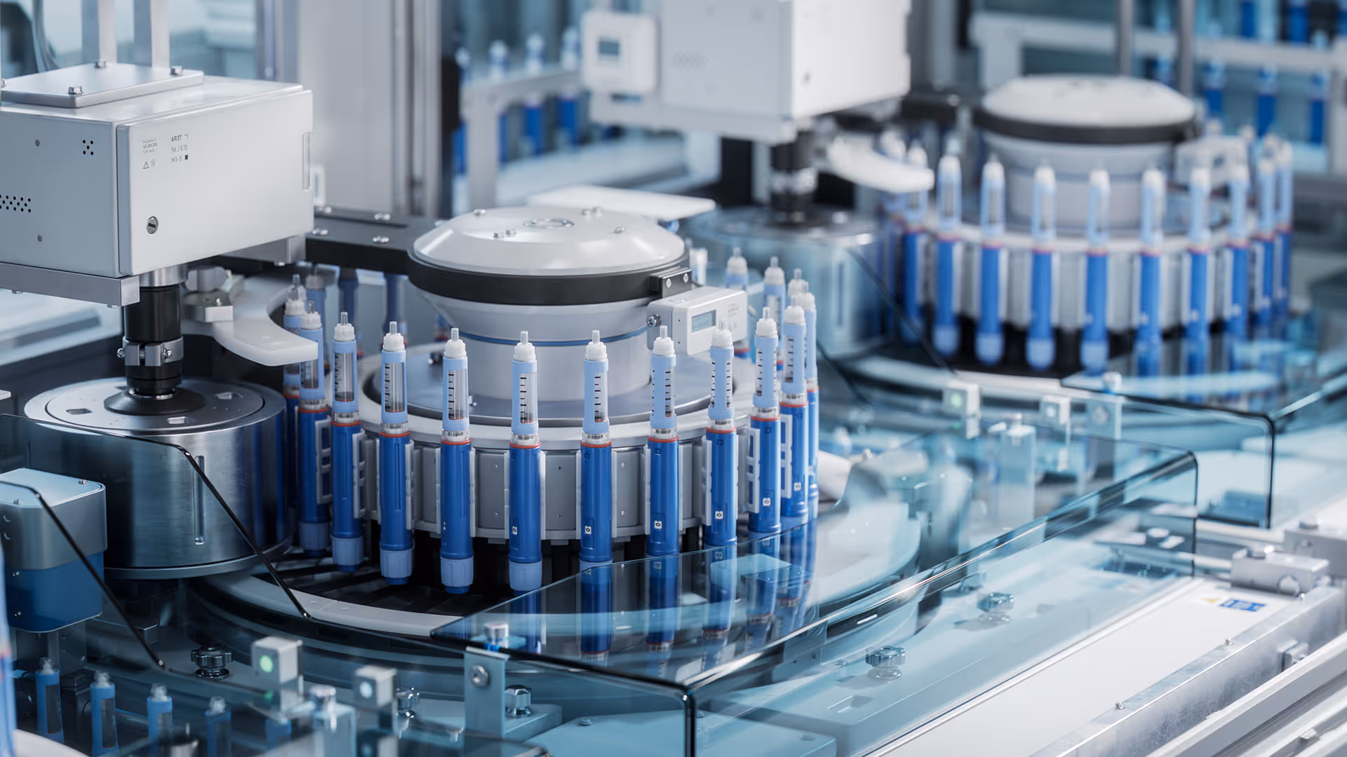 Automated production line with multiple blue and white medical syringes arranged in circular rotary machines.