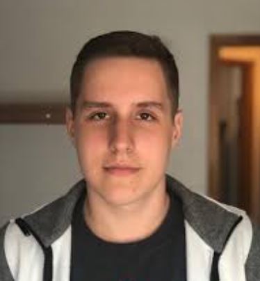 Portrait of a young man with short dark hair wearing a black shirt and white hoodie with gray lining.