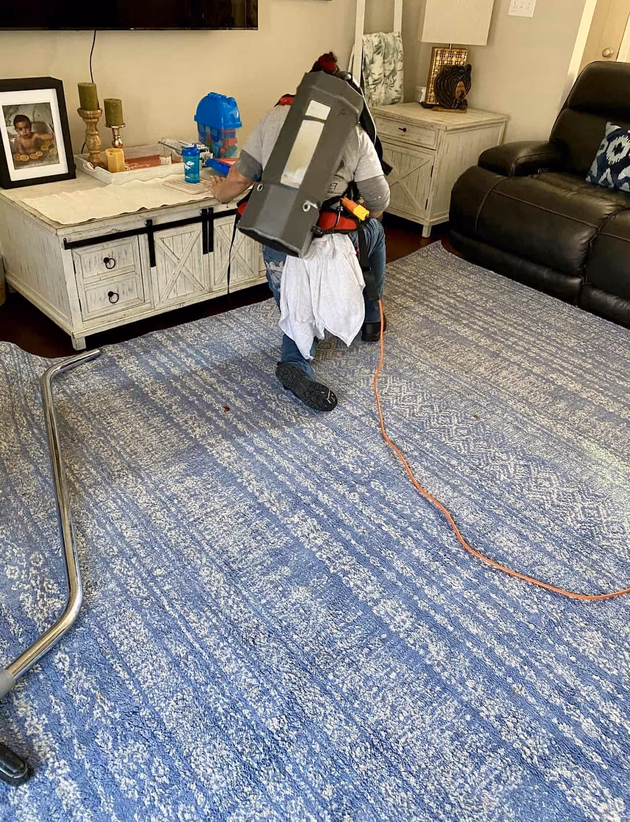 Person kneeling on a blue patterned rug using carpet cleaning equipment in a living room.