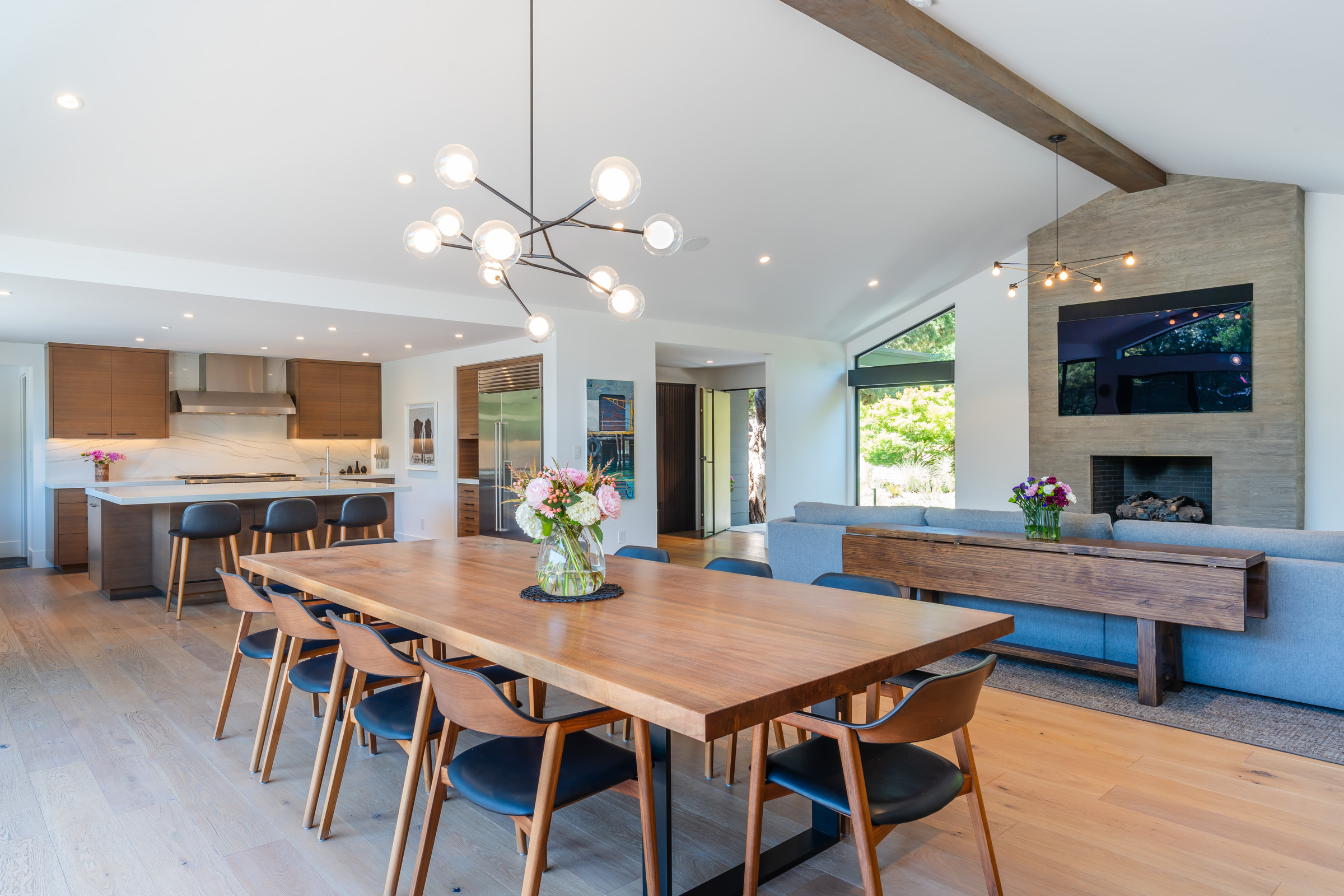 Modern open-concept dining room, kitchen, and living area with vaulted ceiling and tall fireplace in Los Altos Hills.