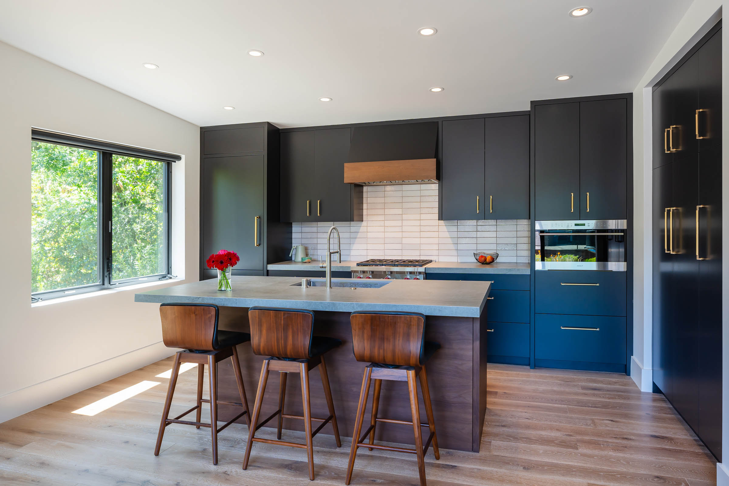 Modern Accessory Dwelling Unit kitchen with dark painted cabinets, wood accents, large island, and a window to a landscaped front yard