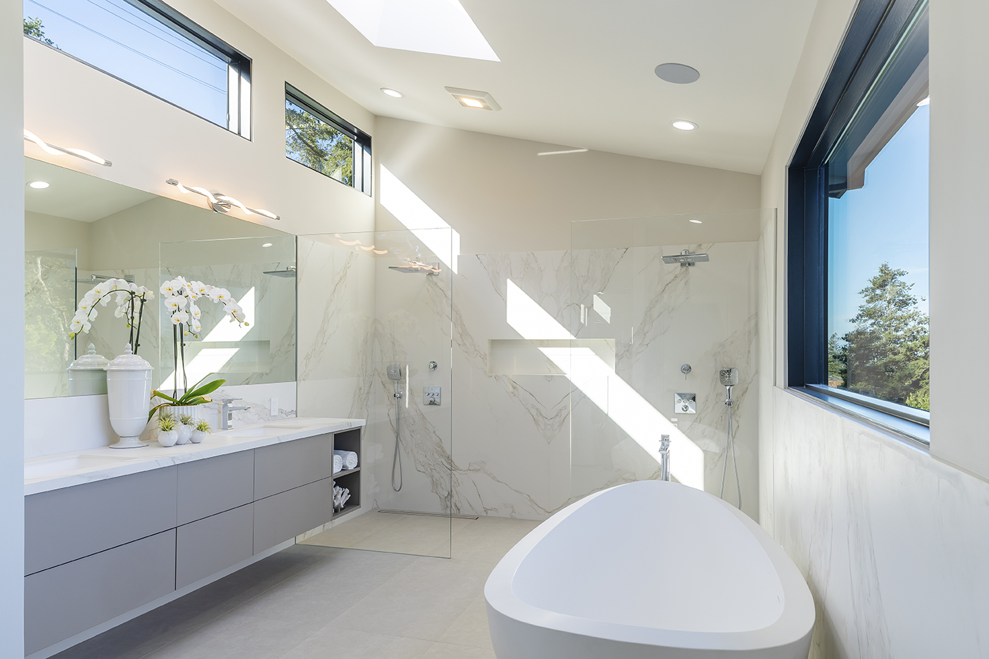 Modern bathroom with freestanding bathtub, double shower with glass panels, large mirror, and gray floating vanity.
