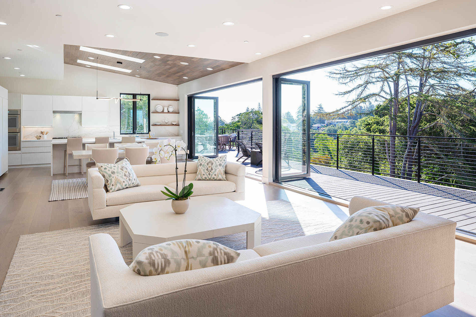 Bright modern living room with bifold glass doors opening to a balcony with views of green trees.