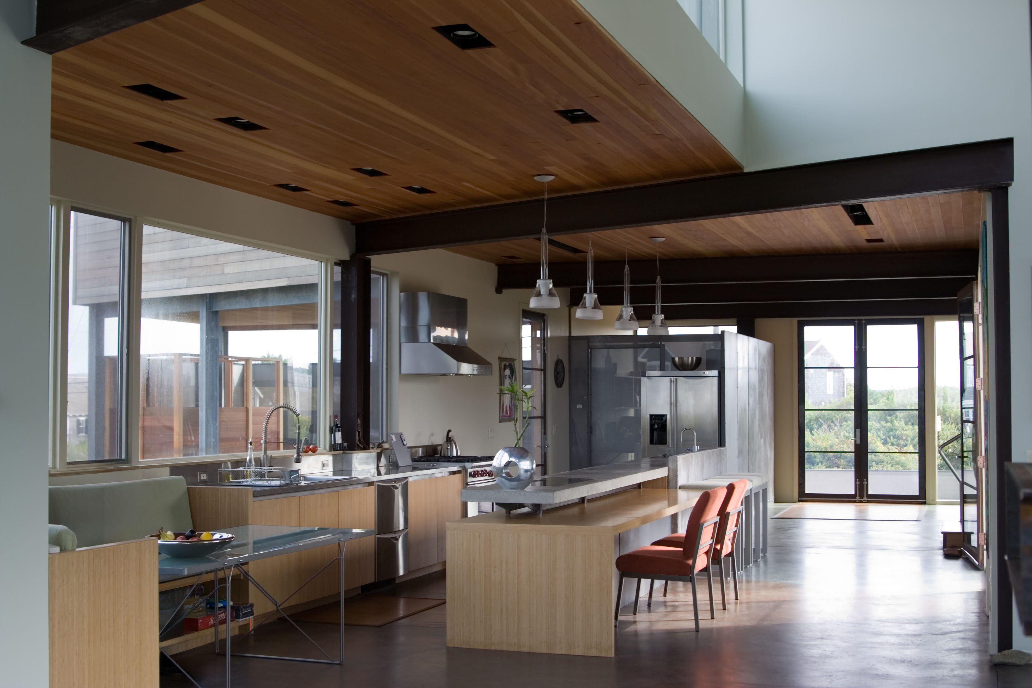 Modern kitchen and dining area with wood ceiling, concrete and wood island, concrete floors, large windows and glass doors.