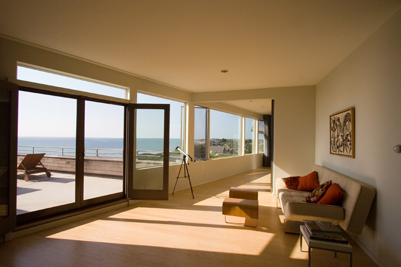 Bright upper level sitting area with large windows and open door leading to a roof deck overlooking the ocean.