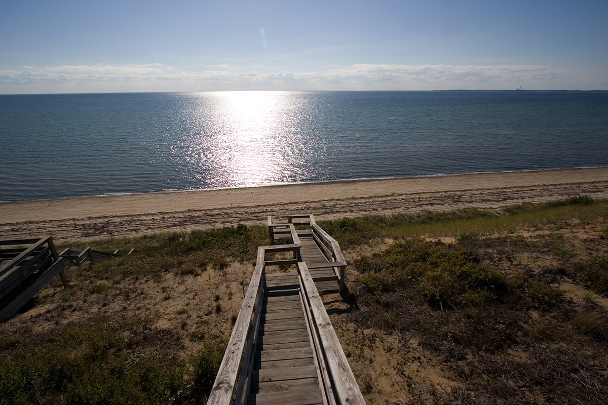 Wooden stairs leading down sandy dunes to Cape Cod Bay with sunlight reflecting off the water.