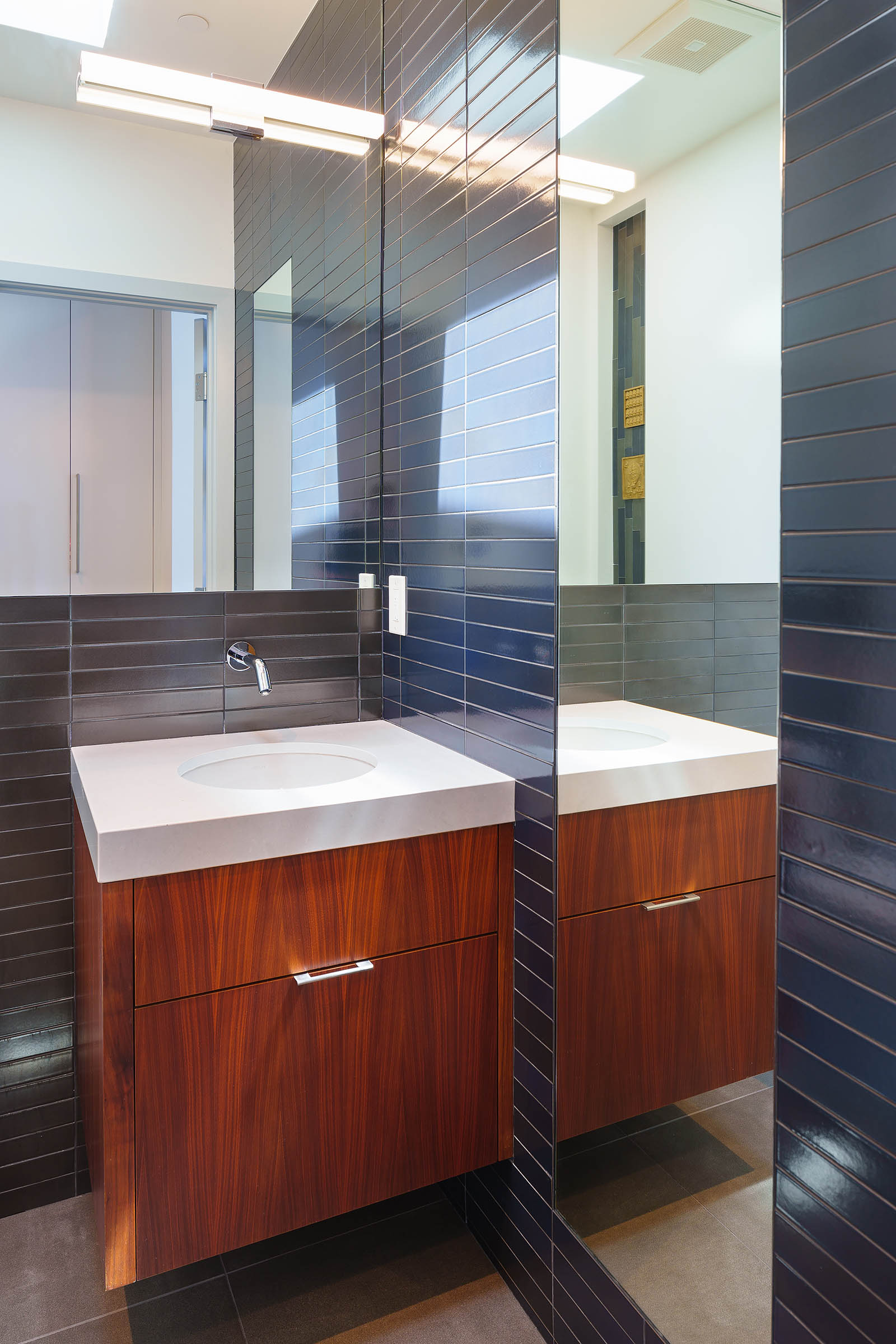 Modern powder room with floating walnut vanity, white quartz countertop, and Heath horizontal tile walls, reflected in a large mirror.