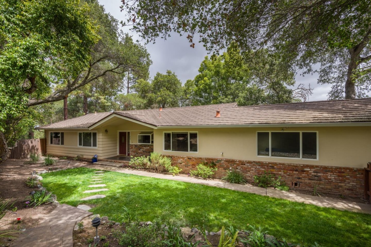Original single-story house set down from the street level, with a low-slope roof and stucco and brick siding