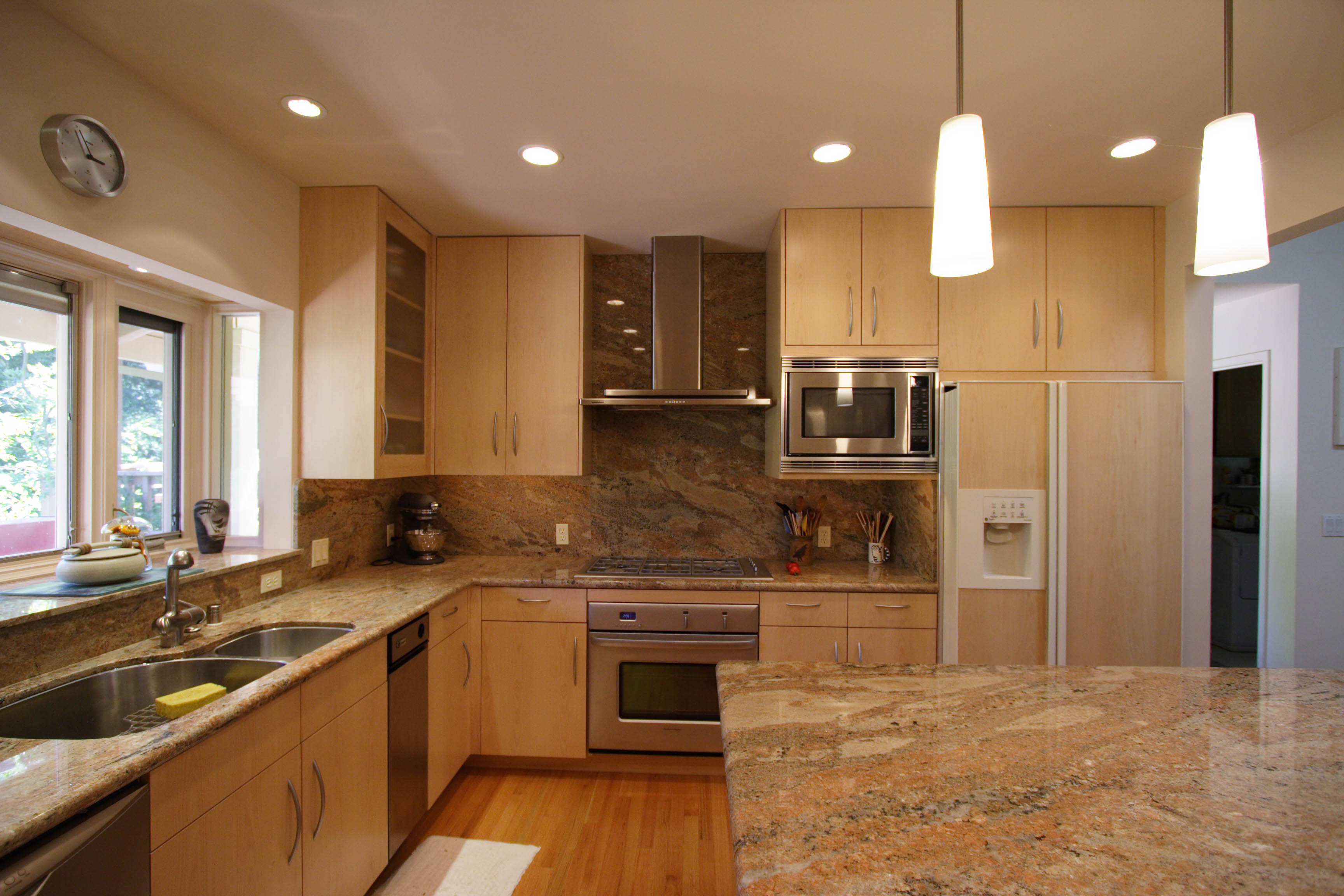 Modern kitchen with light wood cabinets, granite countertops, stainless steel appliances, and two hanging pendant lights.