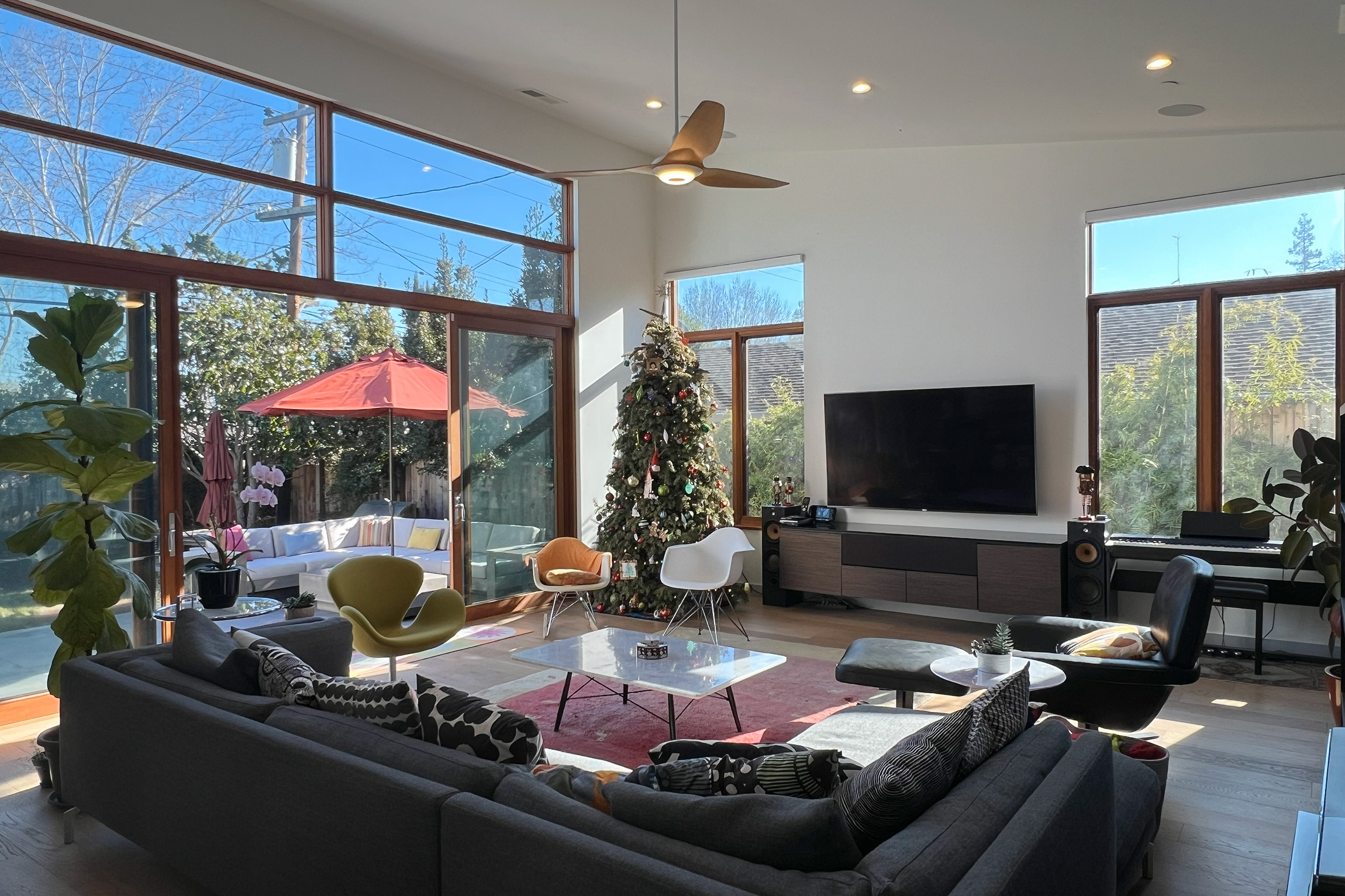 Modern living room with high ceilings, large windows, gray sectional sofa, and a wall-mounted TV.