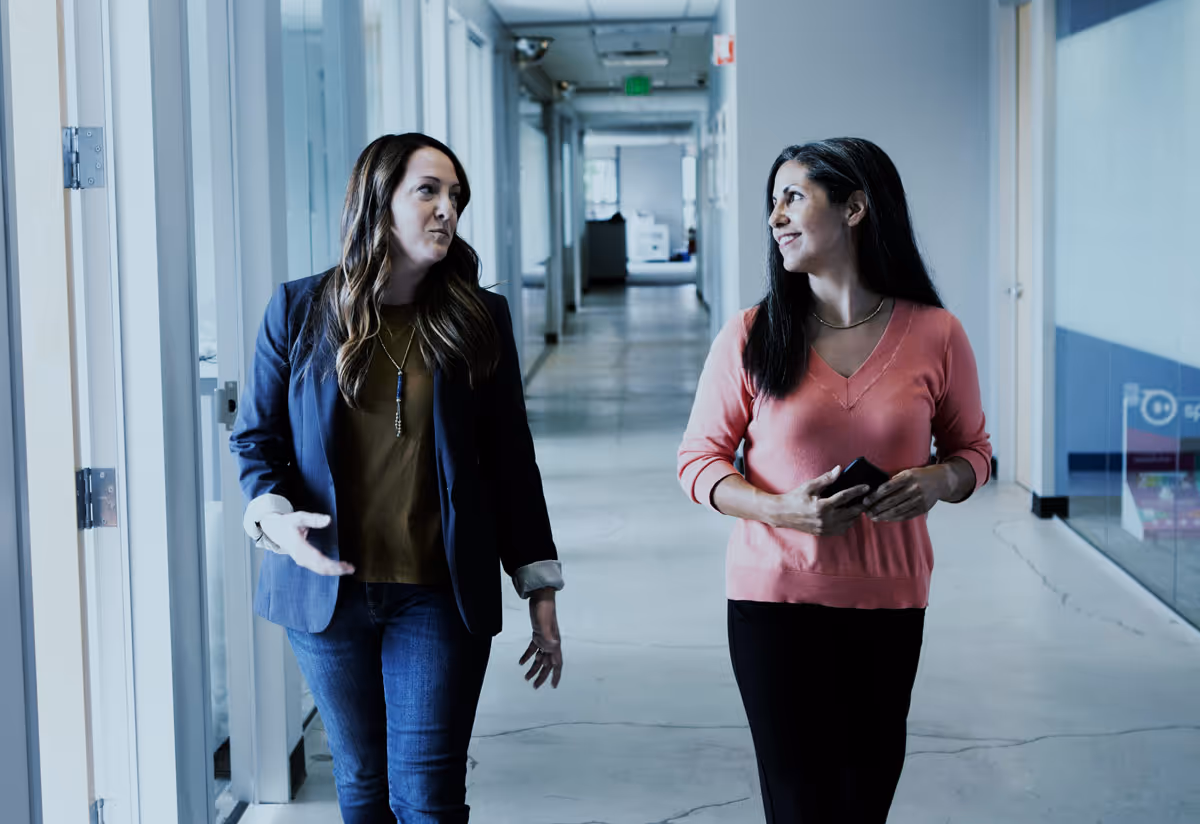 Two coworkers walking and talking in a modern office setting.
