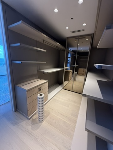 Modern walk-in closet with light wood shelves, drawers, mirrored sliding doors, and recessed ceiling lights.
