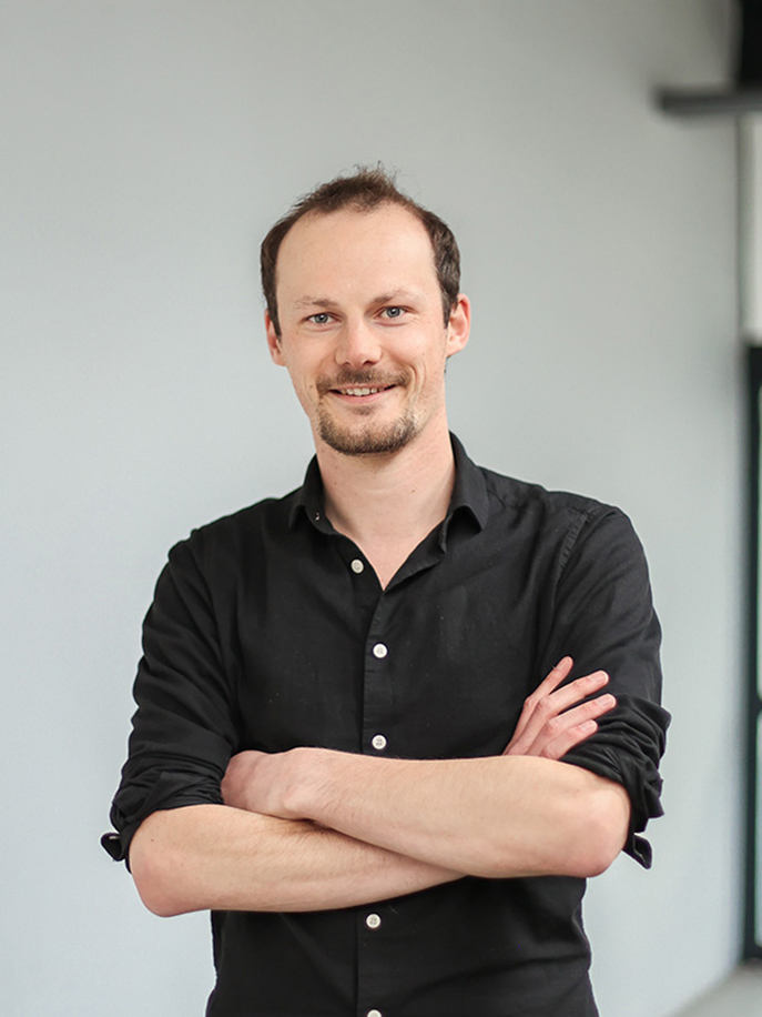 Man met een zwart overhemd staat met gekruiste armen en glimlacht.