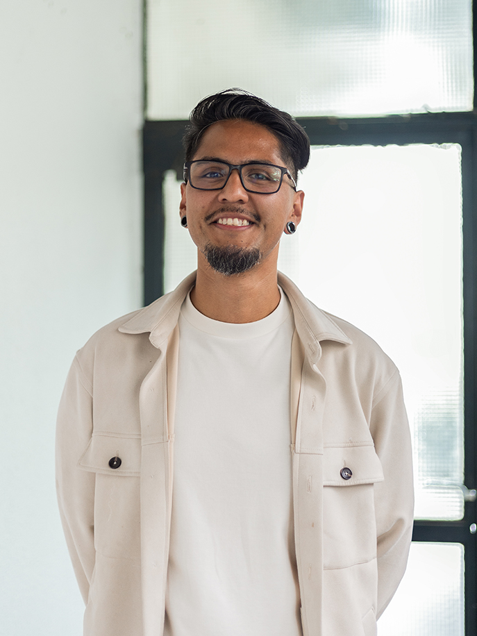 Man met zwarte bril en lichte jas glimlacht voor een raam met melkglas.