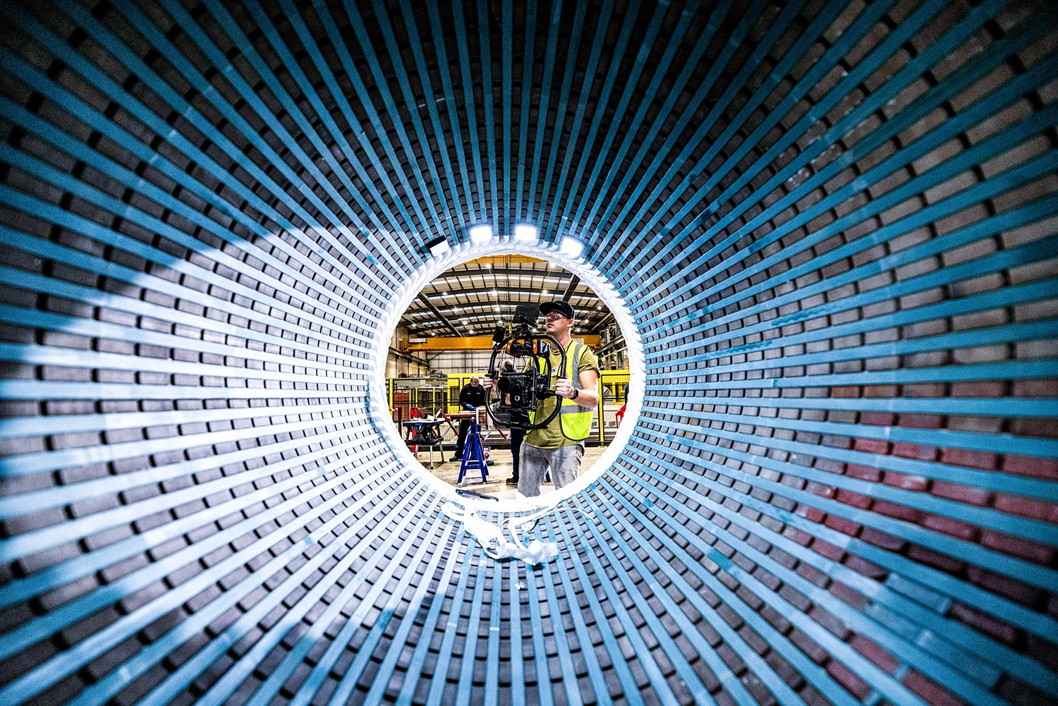 Een man in een reflecterend hesje filmt met een camera binnenin een grote, ronde metalen structuur.