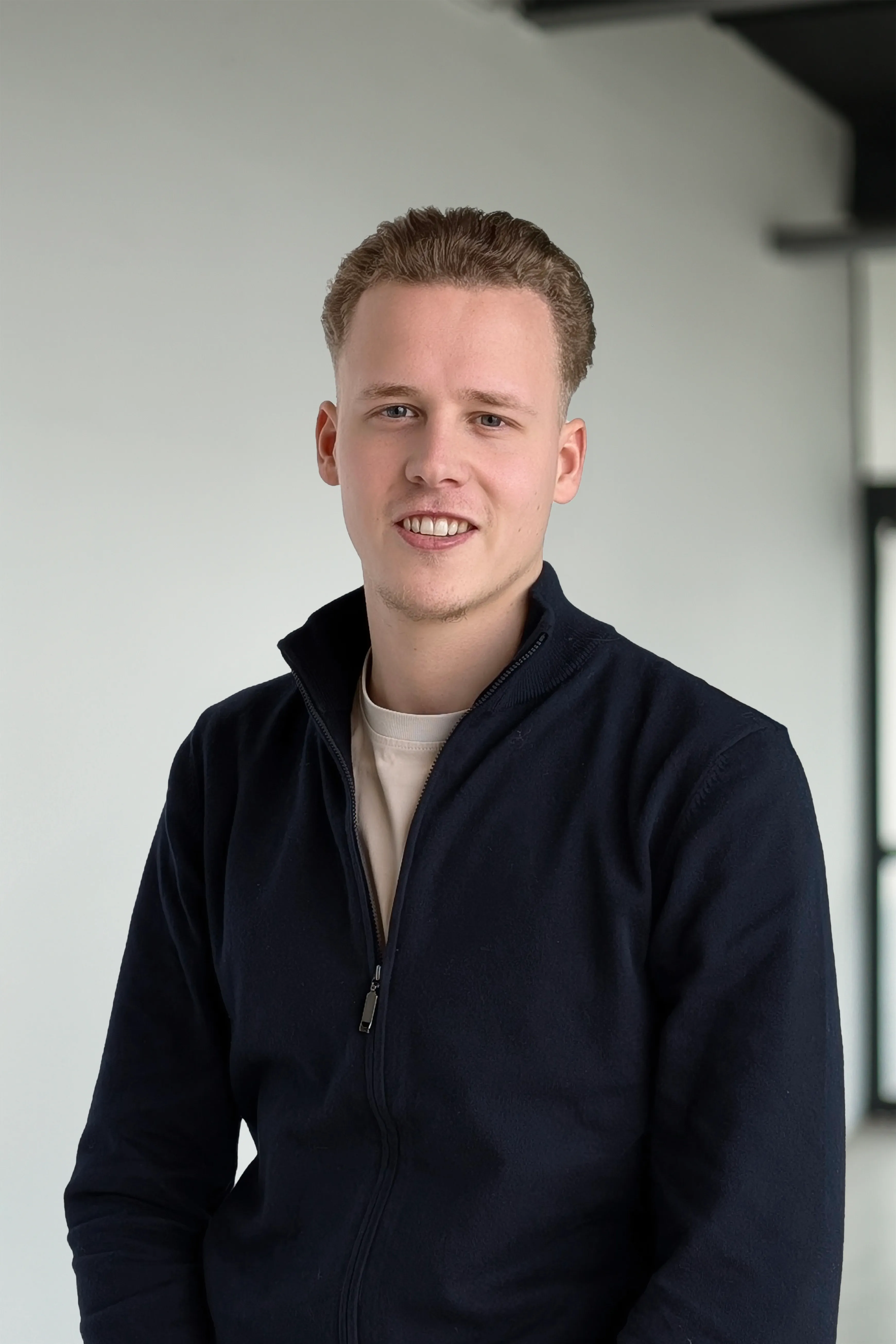 Jonge man lacht naar de camera, hij draagt een donkerblauwe jas met ritssluiting en een licht T-shirt.