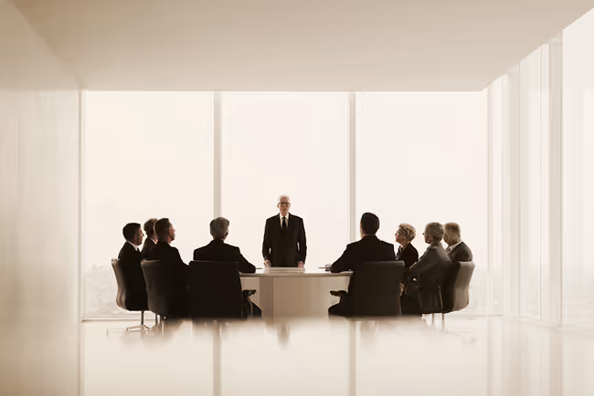 Businessman standing and addressing a group of professionals seated around a conference table in a bright office.