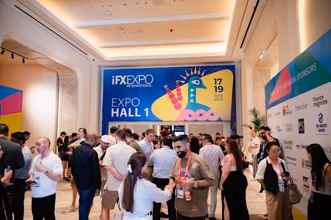 Crowd of people networking inside a well-lit conference hall with a large colorful sign that reads 'iFX Expo International, Expo Hall 1, 17-19 June 2025'.