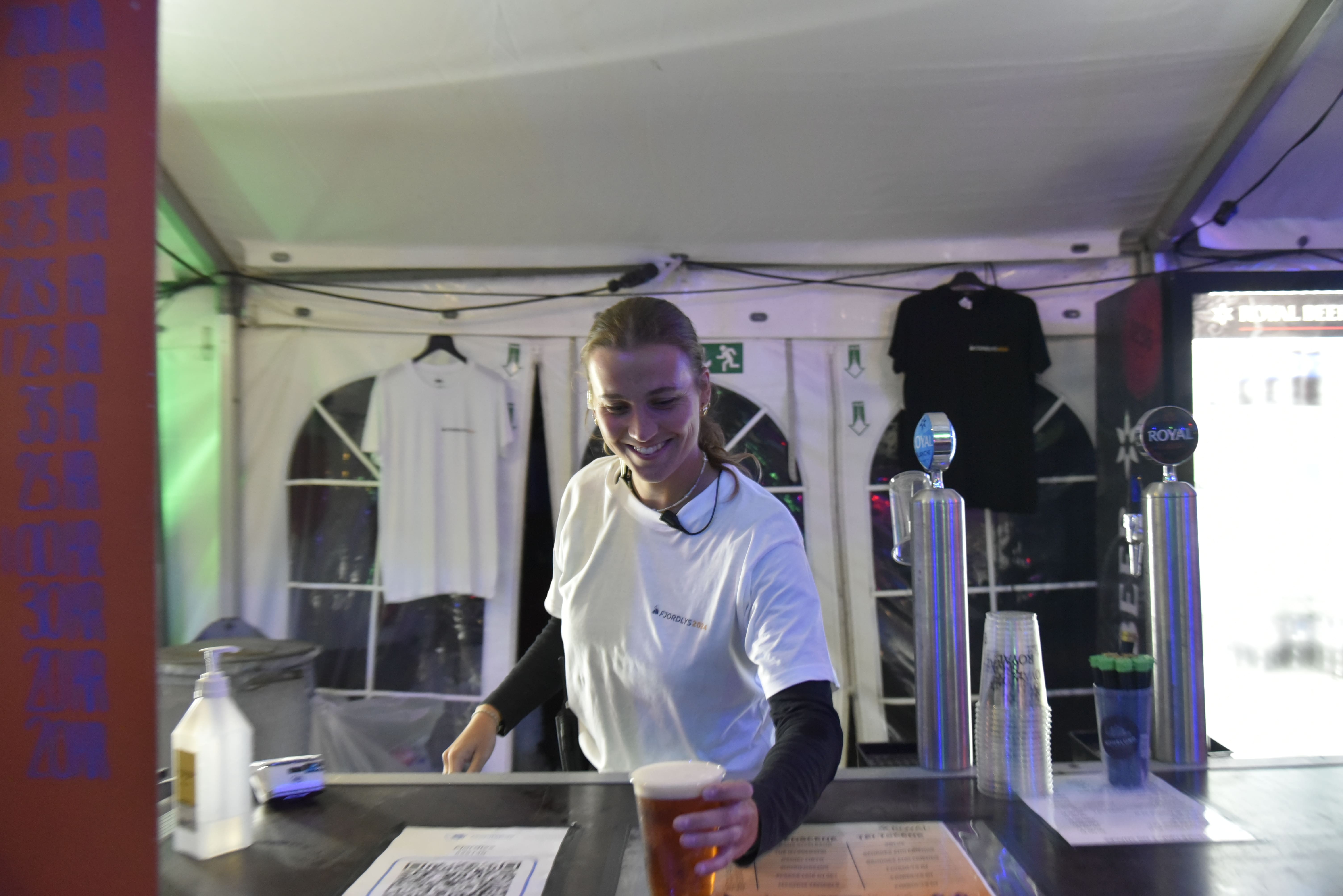 En frivillig på Fjordlys Festival står i baren og er ved at servere en øl til en gæst.