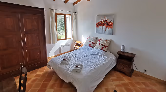 Chambre avec lit double couvert de draps blancs, deux tables de chevet, armoire en bois et fenêtre laissant entrer la lumière naturelle.