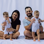 Parents souriants assis sur un lit tenant deux tout-petits habillés de tenues blanches.