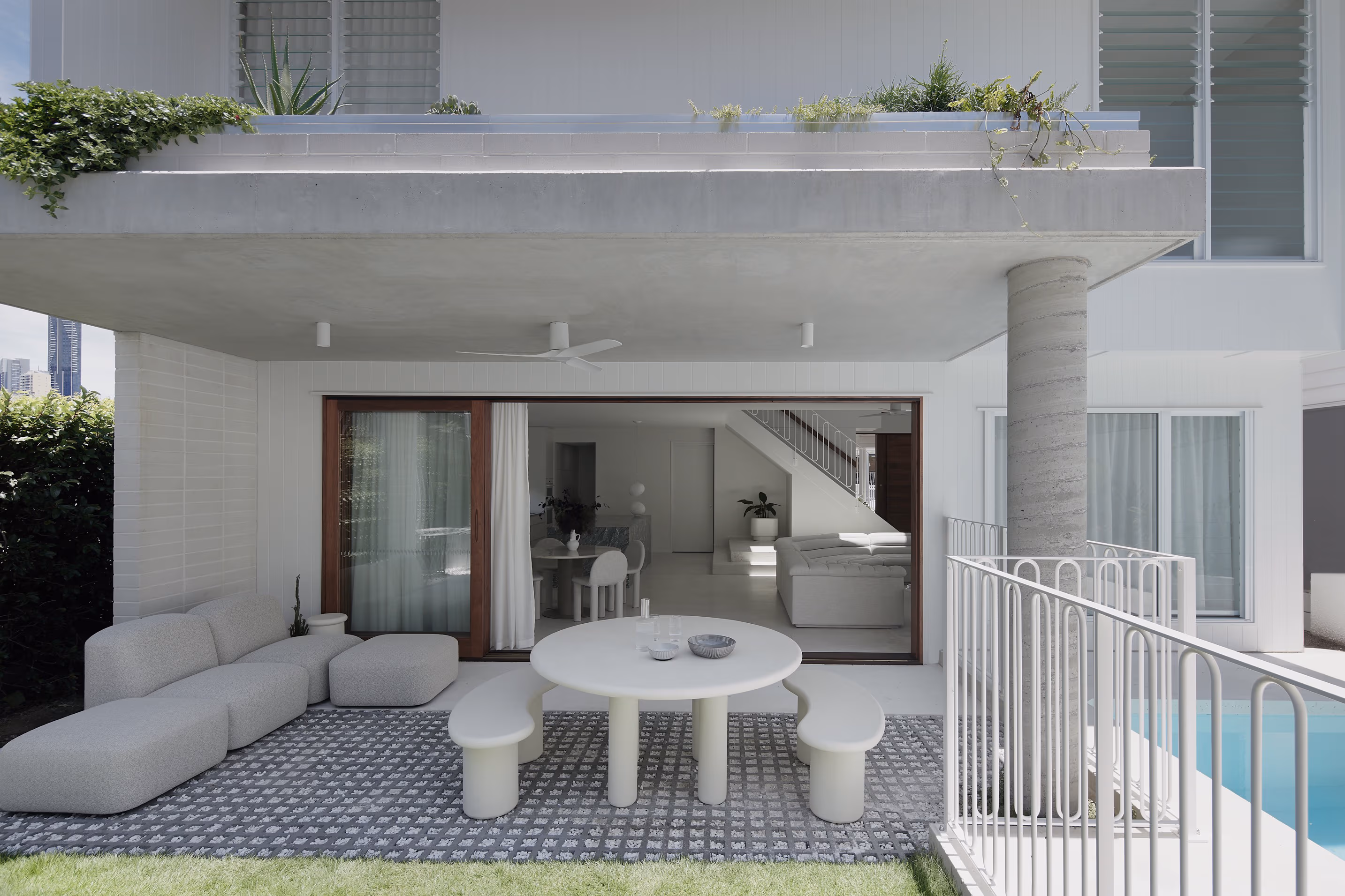 Modern outdoor patio with curved bench sofa, round table with two curved benches, and adjacent pool with white railing.